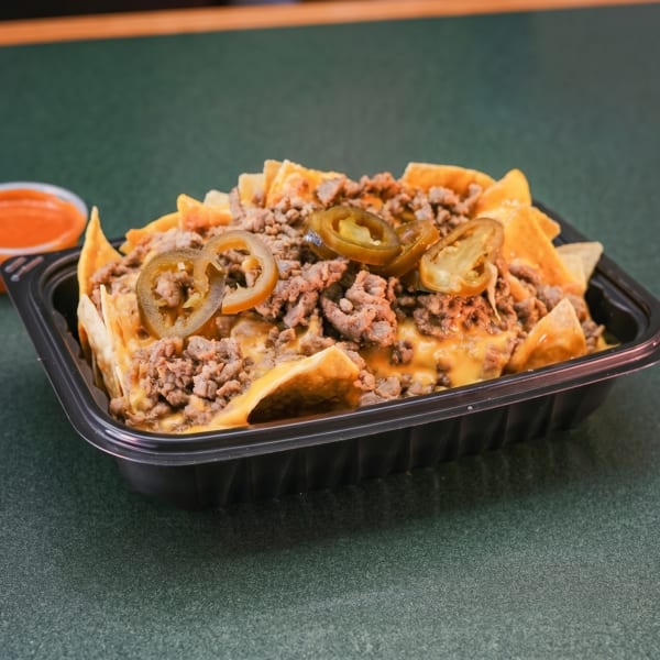 Nachos with ground beef, melted cheese, and sliced jalapeños in a black takeout container.