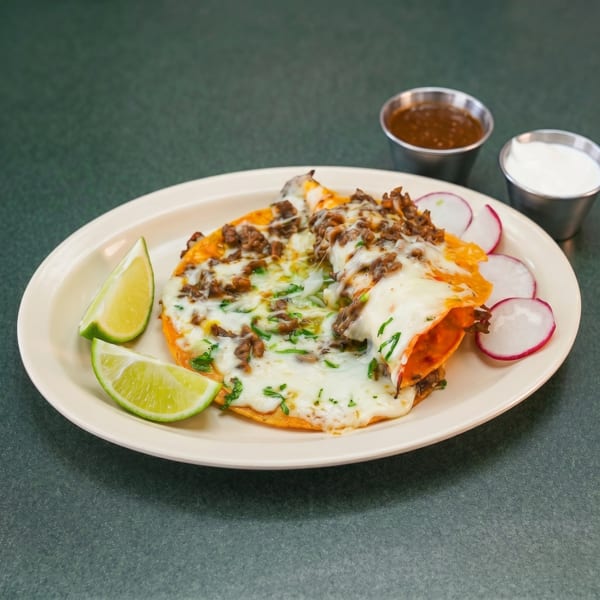 Cheesy beef quesadilla with lime wedges, radish slices, and two dipping sauces on a white plate.