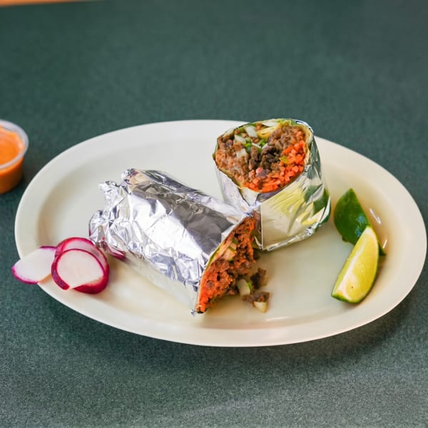 Two foil-wrapped burritos filled with meat and vegetables, served with lime wedges and radish slices.