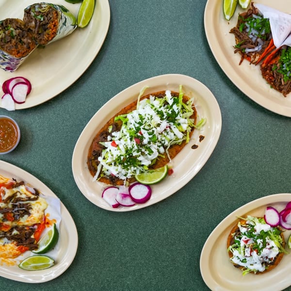 Overhead view of various Mexican dishes including burritos, tacos, sopes, and a huarache on a green table.