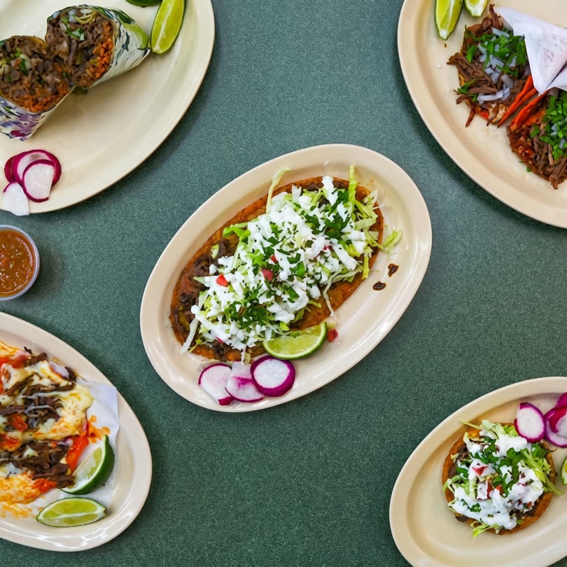 Overhead view of various Mexican dishes including burritos, tacos, sopes, and a huarache on a green table.