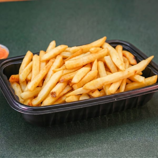 Golden french fries in a black plastic container on a green textured surface.