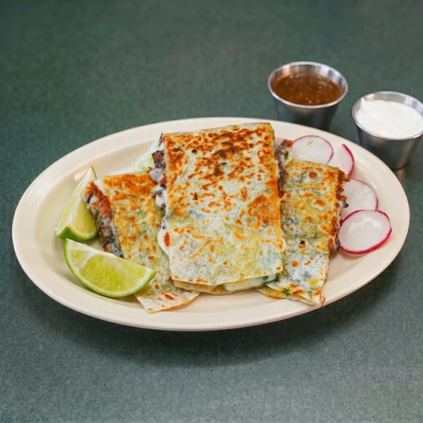 Three cheesy quesadillas with lime wedges and radish slices, served with salsa and sour cream.