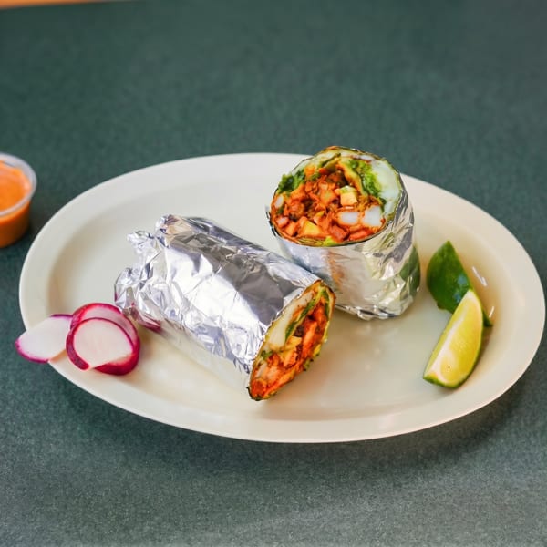 Two foil-wrapped burritos with red meat, green sauce, and white cheese, garnished with radishes and limes.